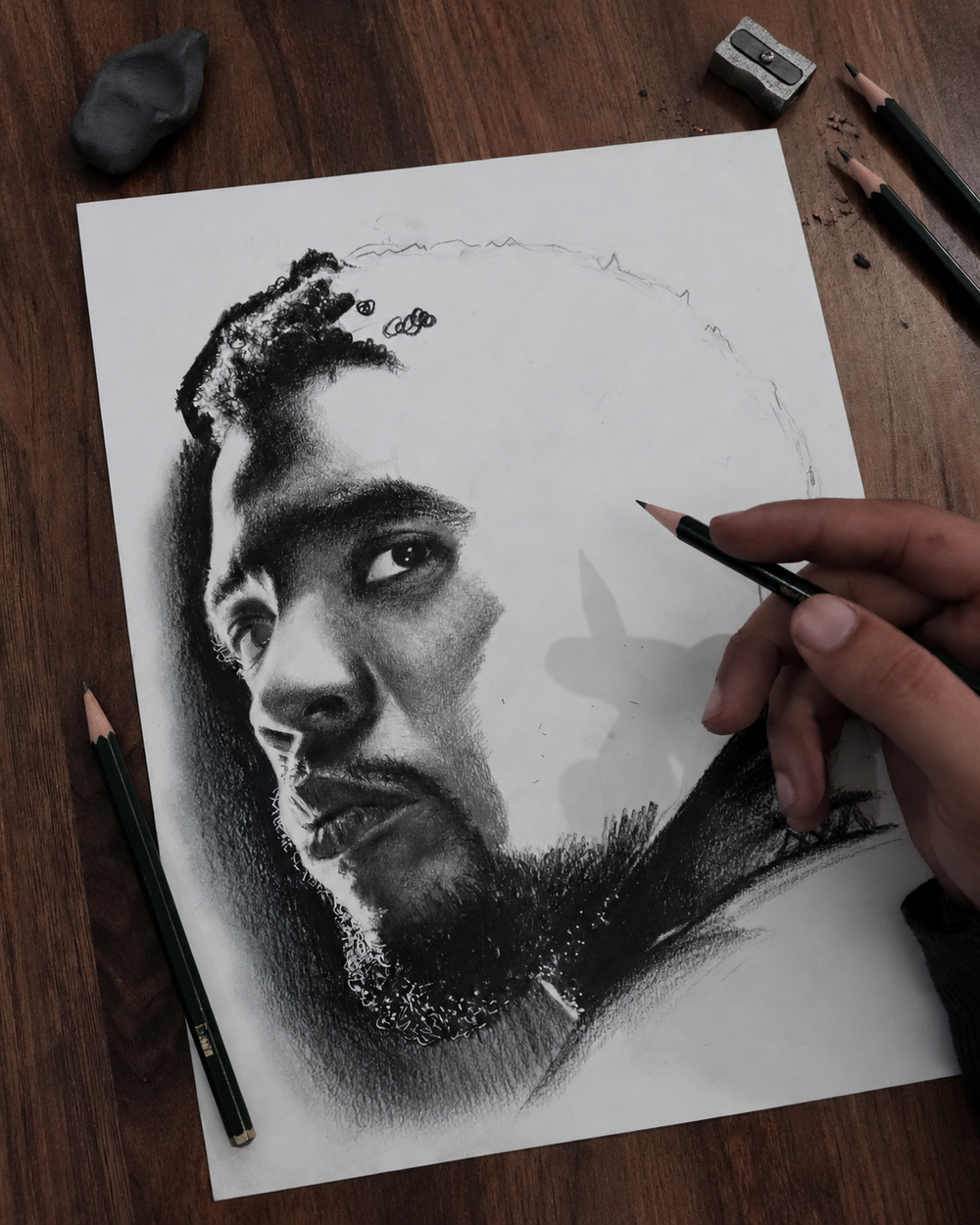 Karim's hand drawing a realistic charcoal and pencil portrait